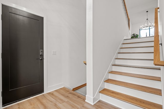 staircase featuring baseboards, an inviting chandelier, and wood finished floors