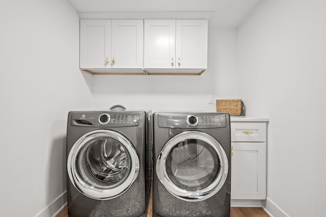 laundry room featuring cabinet space, baseboards, washing machine and dryer, and wood finished floors