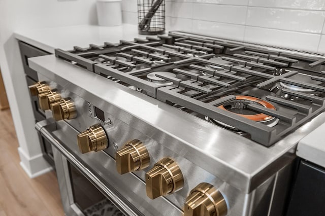 details with high end range, wood finished floors, and backsplash