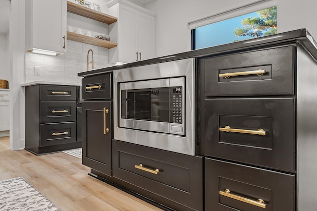 kitchen featuring light wood-style flooring, tasteful backsplash, white cabinetry, open shelves, and stainless steel microwave