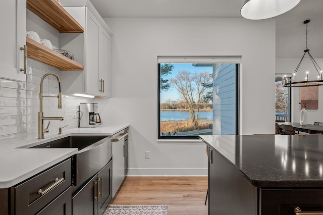 kitchen with light wood-style floors, open shelves, a chandelier, a sink, and backsplash