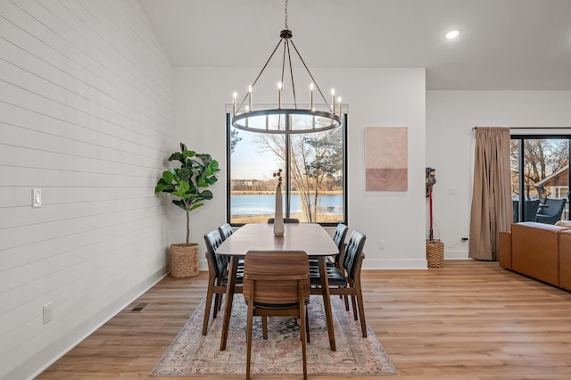 dining space featuring a water view, wood walls, light wood-style floors, and an inviting chandelier