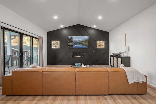 living room featuring light wood-style flooring, an accent wall, baseboards, and lofted ceiling