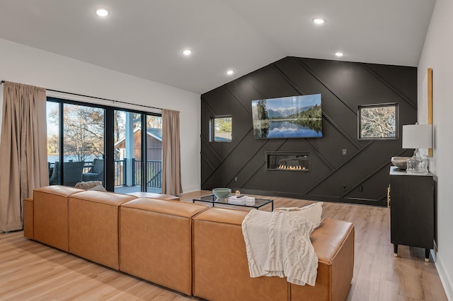 living room with an accent wall, light wood-style floors, recessed lighting, vaulted ceiling, and a large fireplace