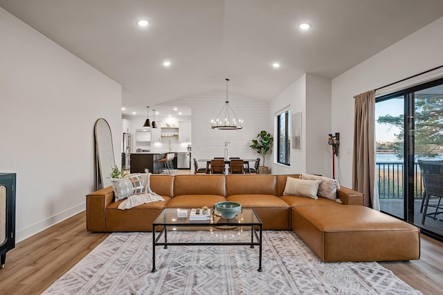 living area featuring a notable chandelier, light wood-style flooring, baseboards, and vaulted ceiling