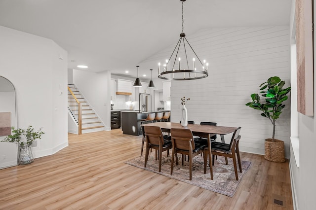 dining area with a chandelier, stairway, light wood-style flooring, wooden walls, and lofted ceiling