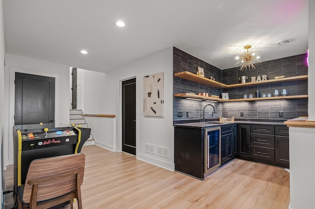 bar with wine cooler, decorative backsplash, light wood finished floors, and indoor wet bar