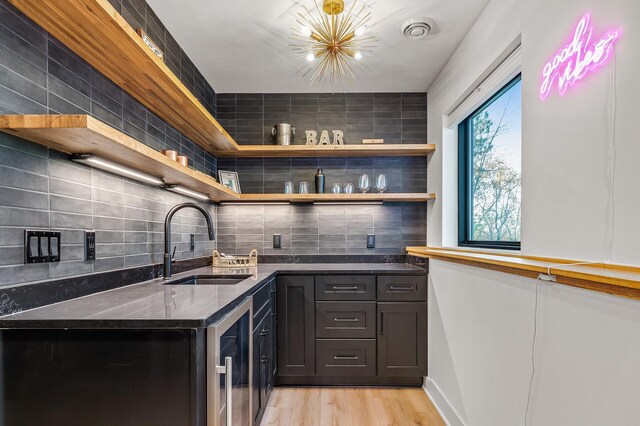 bar featuring a sink, tasteful backsplash, a notable chandelier, and light wood-style flooring