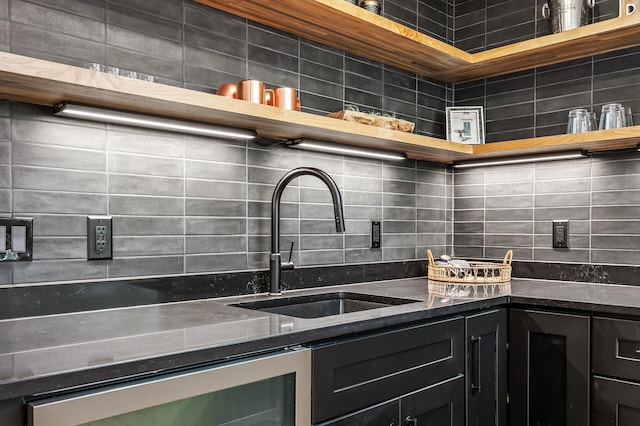 kitchen featuring dark stone countertops, open shelves, a sink, dark cabinetry, and backsplash