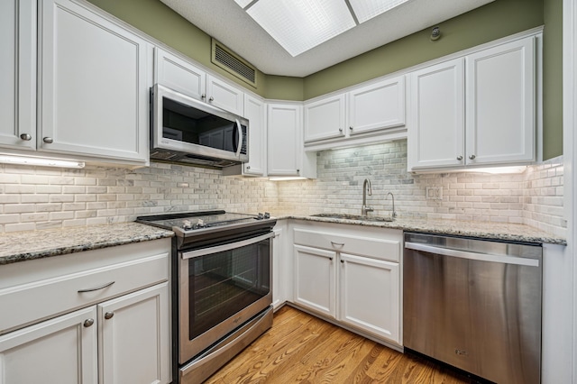 2950 Dean Pkwy Unit 2005, Minneapolis, MN 55416 - kitchen with appliances with stainless steel finishes, a sink, white cabinets, light wood-type flooring, and decorative backsplash