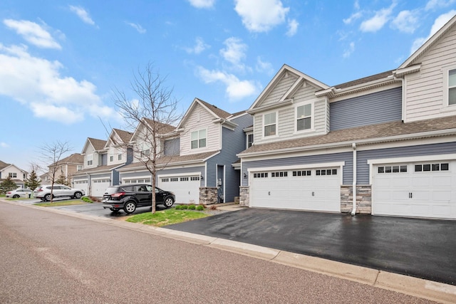 townhome / multi-family property featuring stone siding, a shingled roof, an attached garage, driveway, and a residential view