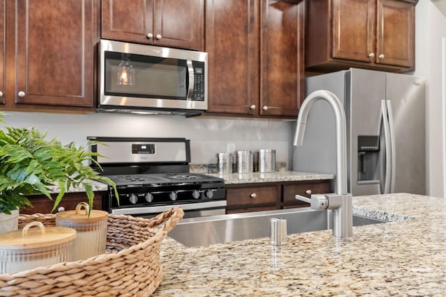 kitchen with appliances with stainless steel finishes, light stone counters, and dark brown cabinets