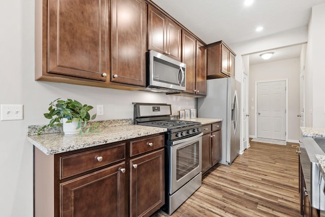 kitchen with dark brown cabinetry, appliances with stainless steel finishes, light stone counters, light wood-style floors, and recessed lighting