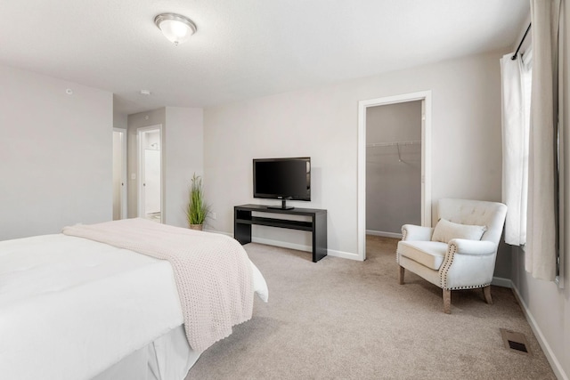 bedroom featuring a walk in closet, visible vents, baseboards, a closet, and light carpet