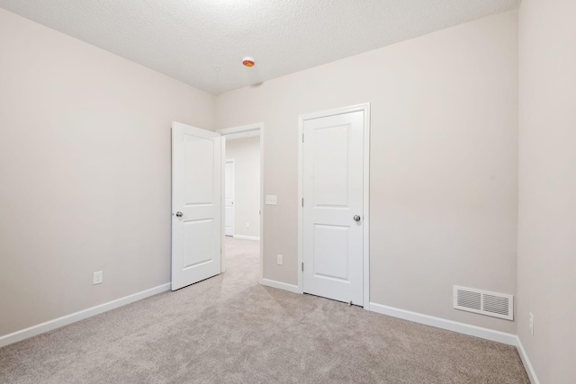 unfurnished bedroom with visible vents, a textured ceiling, baseboards, and light carpet