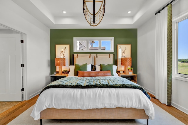 bedroom featuring a tray ceiling, wood finished floors, and multiple windows