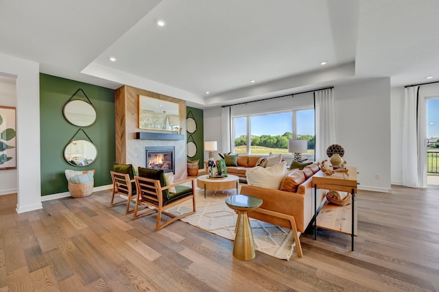living room featuring light wood finished floors, a wealth of natural light, recessed lighting, a large fireplace, and a raised ceiling