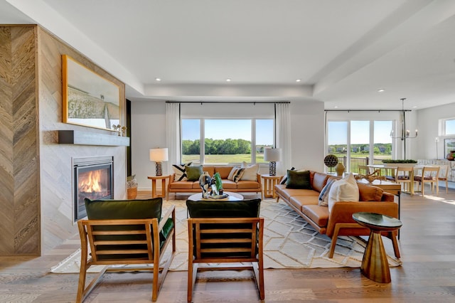 living room with an inviting chandelier, a glass covered fireplace, wood finished floors, and recessed lighting