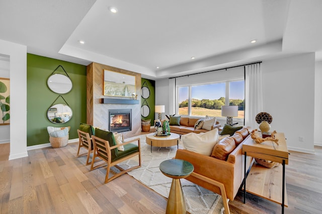 living area with light wood-style floors, a tray ceiling, a fireplace, baseboards, and recessed lighting