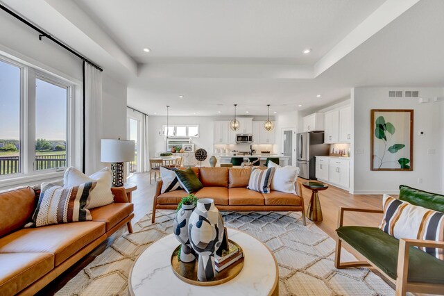 living area featuring recessed lighting, visible vents, light wood finished floors, and a tray ceiling