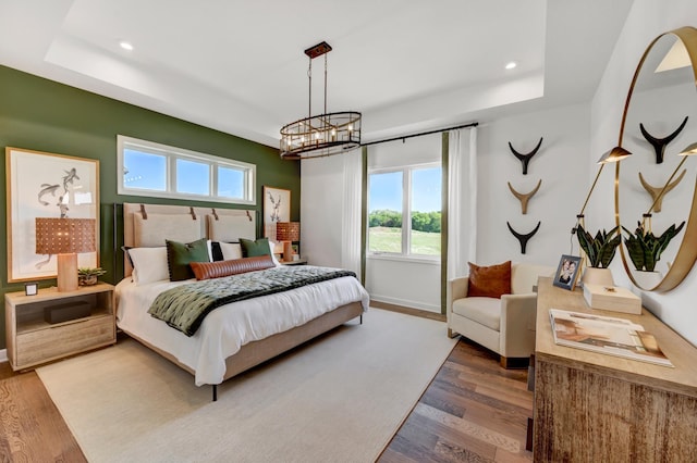 bedroom with a raised ceiling, wood finished floors, a notable chandelier, and multiple windows