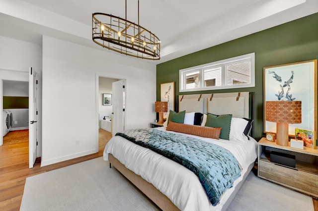 bedroom with wood finished floors, connected bathroom, baseboards, a notable chandelier, and washer / clothes dryer