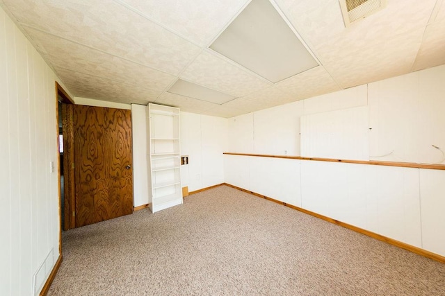 spare room featuring light colored carpet, visible vents, baseboards, and wooden walls