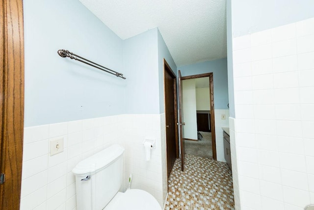 bathroom featuring tile walls, a textured ceiling, wainscoting, and toilet