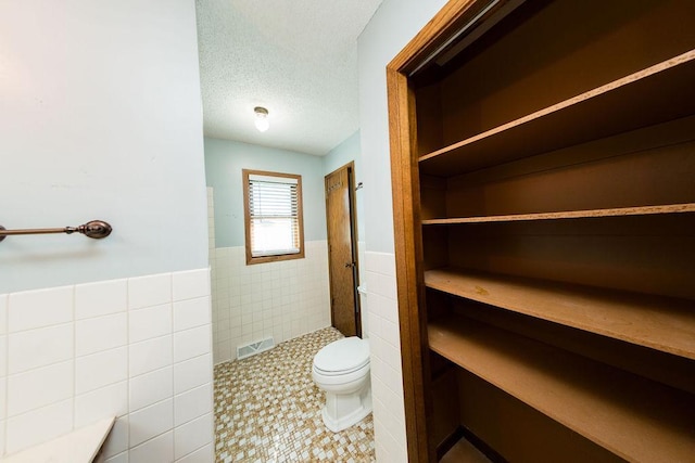 full bath with tile walls, toilet, wainscoting, a tile shower, and tile patterned floors