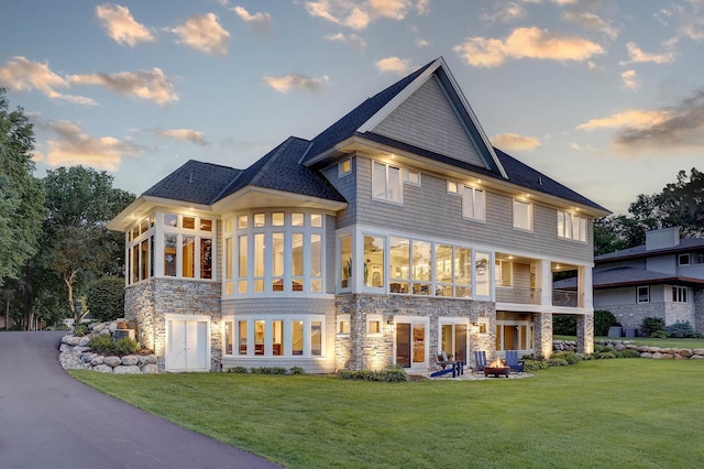 2625 Woodbridge Rd, Minnetonka Beach, MN 55391 - back of property at dusk featuring stone siding, a lawn, a sunroom, and a patio