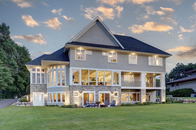 2625 Woodbridge Rd, Minnetonka Beach, MN 55391 - back of property at dusk featuring stone siding, a yard, a sunroom, roof with shingles, and a balcony