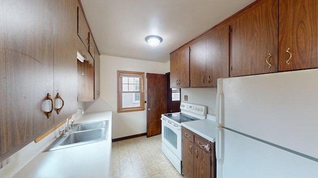kitchen featuring light floors, light countertops, a sink, white appliances, and baseboards
