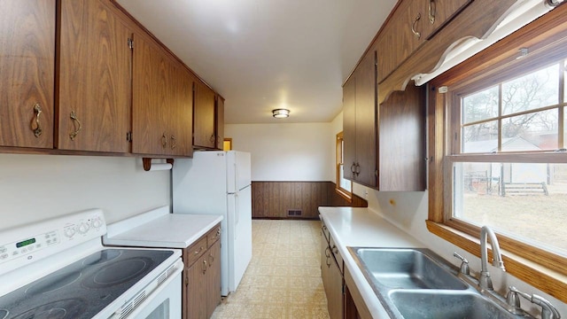kitchen featuring light floors, light countertops, a sink, white appliances, and wainscoting