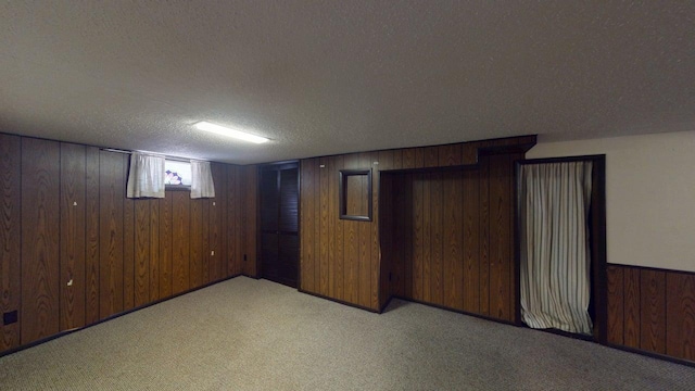 below grade area featuring light carpet, a textured ceiling, and wooden walls