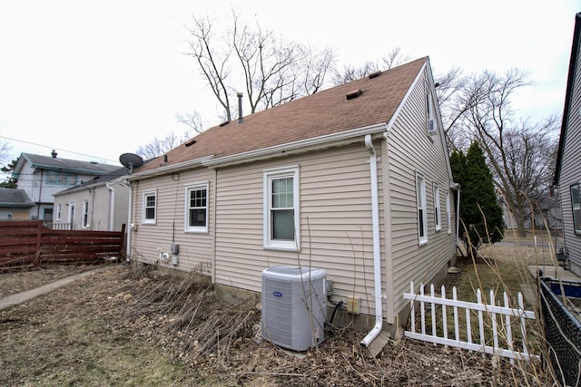 rear view of property with fence, roof with shingles, and central AC unit