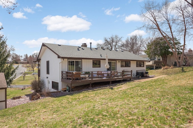 back of property with a yard, a deck, a chimney, and roof with shingles