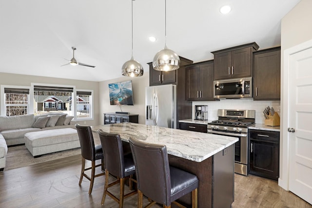 24235 143rd St NW, Zimmerman, MN 55398 - kitchen featuring appliances with stainless steel finishes, a kitchen breakfast bar, dark brown cabinetry, a ceiling fan, and open floor plan