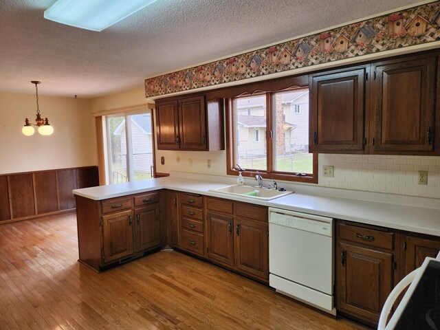 kitchen with a peninsula, light countertops, light wood finished floors, dishwasher, and a sink