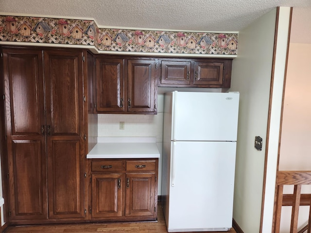 kitchen featuring dark brown cabinetry, light countertops, freestanding refrigerator, and a textured ceiling