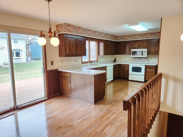 kitchen with white appliances, light wood-style flooring, a peninsula, a wainscoted wall, and light countertops