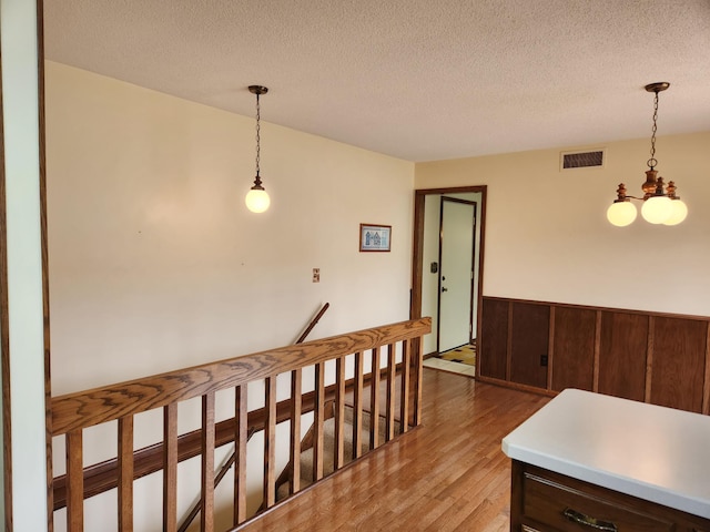 corridor featuring an inviting chandelier, a textured ceiling, visible vents, a wainscoted wall, and light wood finished floors