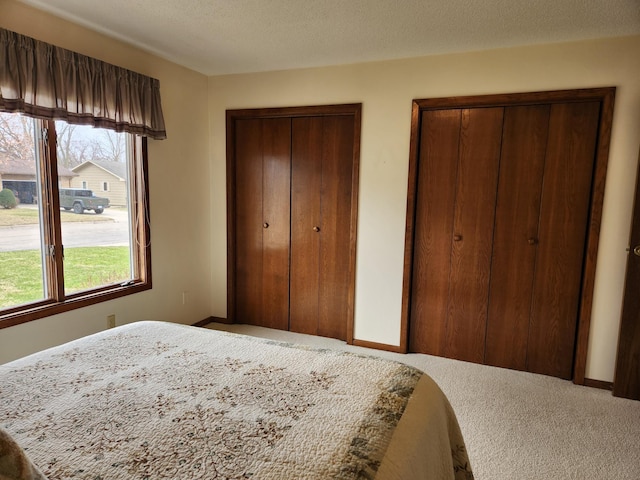 carpeted bedroom featuring two closets, baseboards, and a textured ceiling