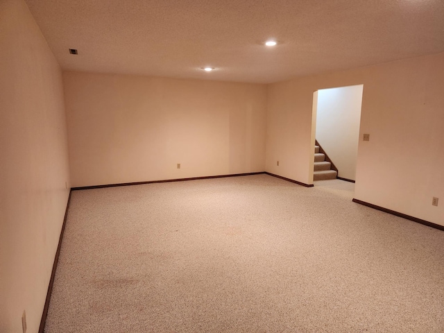 carpeted spare room featuring baseboards, stairway, and a textured ceiling