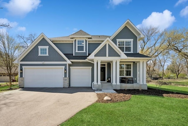 craftsman inspired home featuring covered porch, roof with shingles, a front yard, aphalt driveway, and an attached garage
