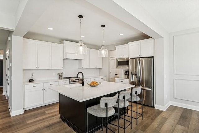 kitchen featuring baseboards, a center island with sink, light countertops, a sink, and stainless steel appliances