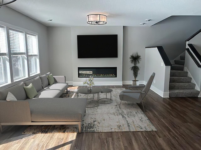 living area featuring a glass covered fireplace, baseboards, stairway, and wood finished floors