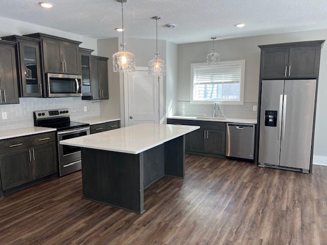 kitchen with decorative backsplash, glass insert cabinets, dark wood-style floors, a sink, and appliances with stainless steel finishes