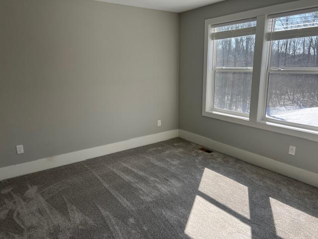 spare room featuring baseboards, dark carpet, and visible vents