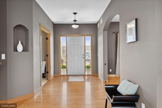 foyer entrance featuring visible vents, light wood-style flooring, arched walkways, and baseboards