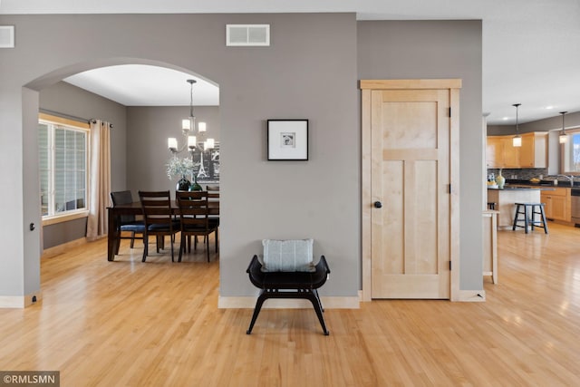 dining room featuring arched walkways, light wood finished floors, visible vents, and baseboards